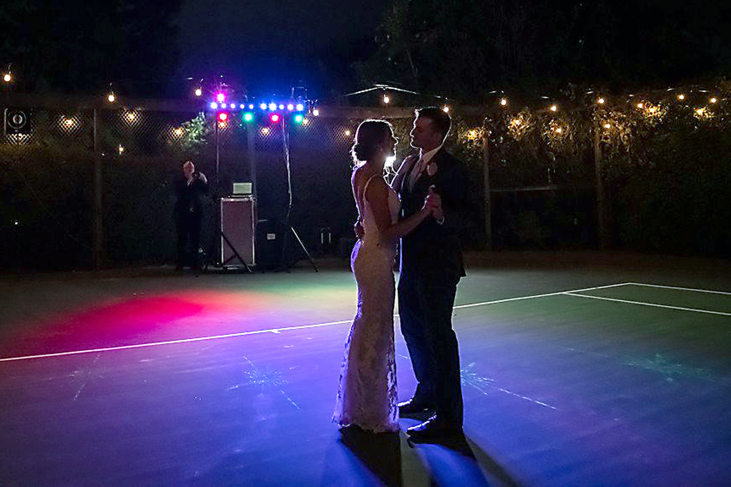 Bride and groom outdoor first dance under colorful DJ lighting on a tennis court in Northern California