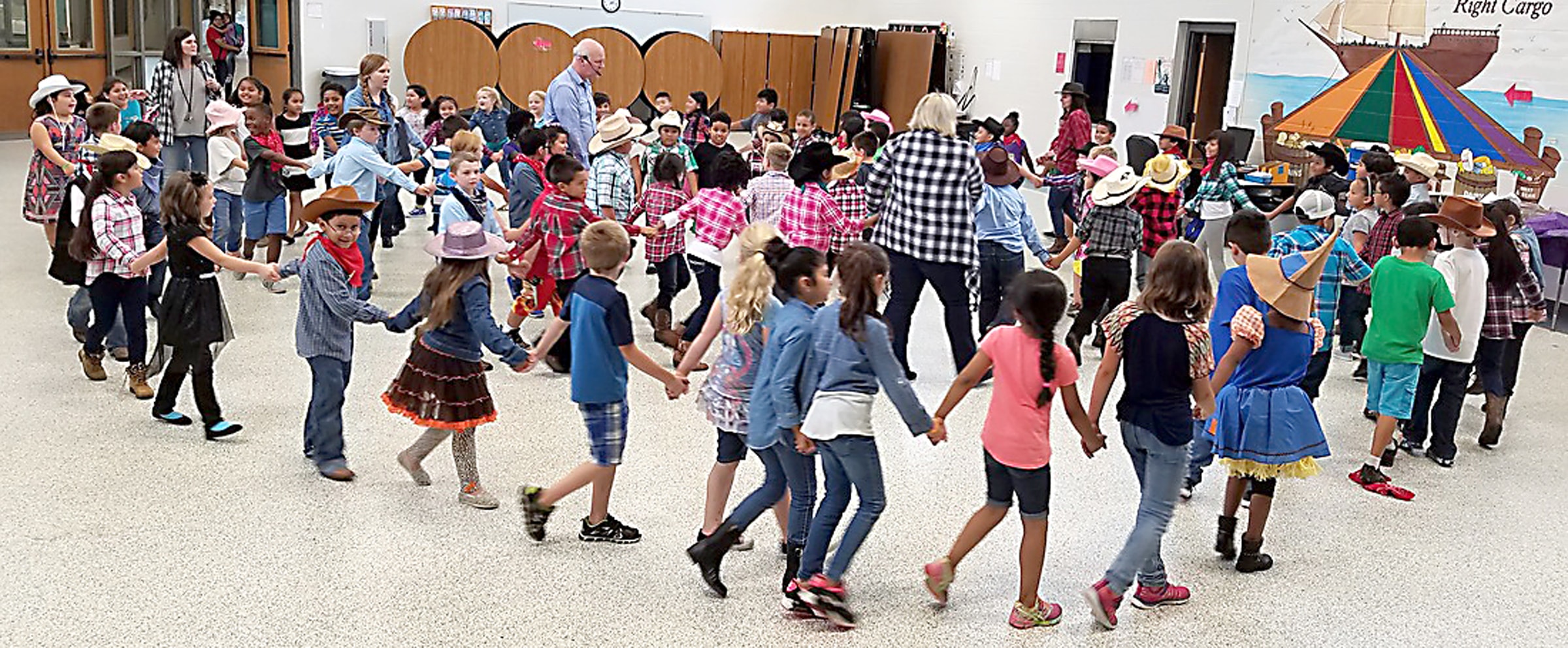 Second grade students in cowboy hats holding hands in a circle at an annual hoedown in Rogers, Arkansas